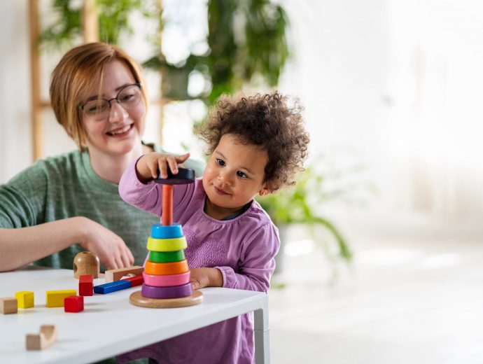 Mother looking at a child playing with an educational didactic toy. Preschool teacher with a child playing with didactic toys. Mixed race family