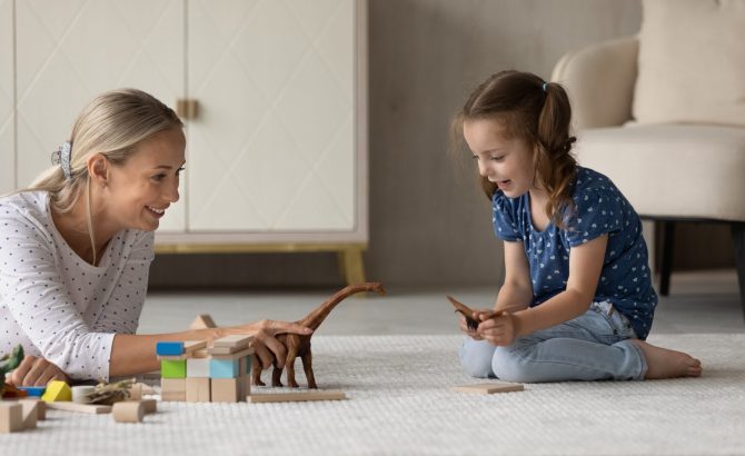 Cute little 7s girl child sit on floor play with loving young Caucasian mother enjoy family leisure weekend. Caring mom and small daughter engaged in playful activity with animal toys together.